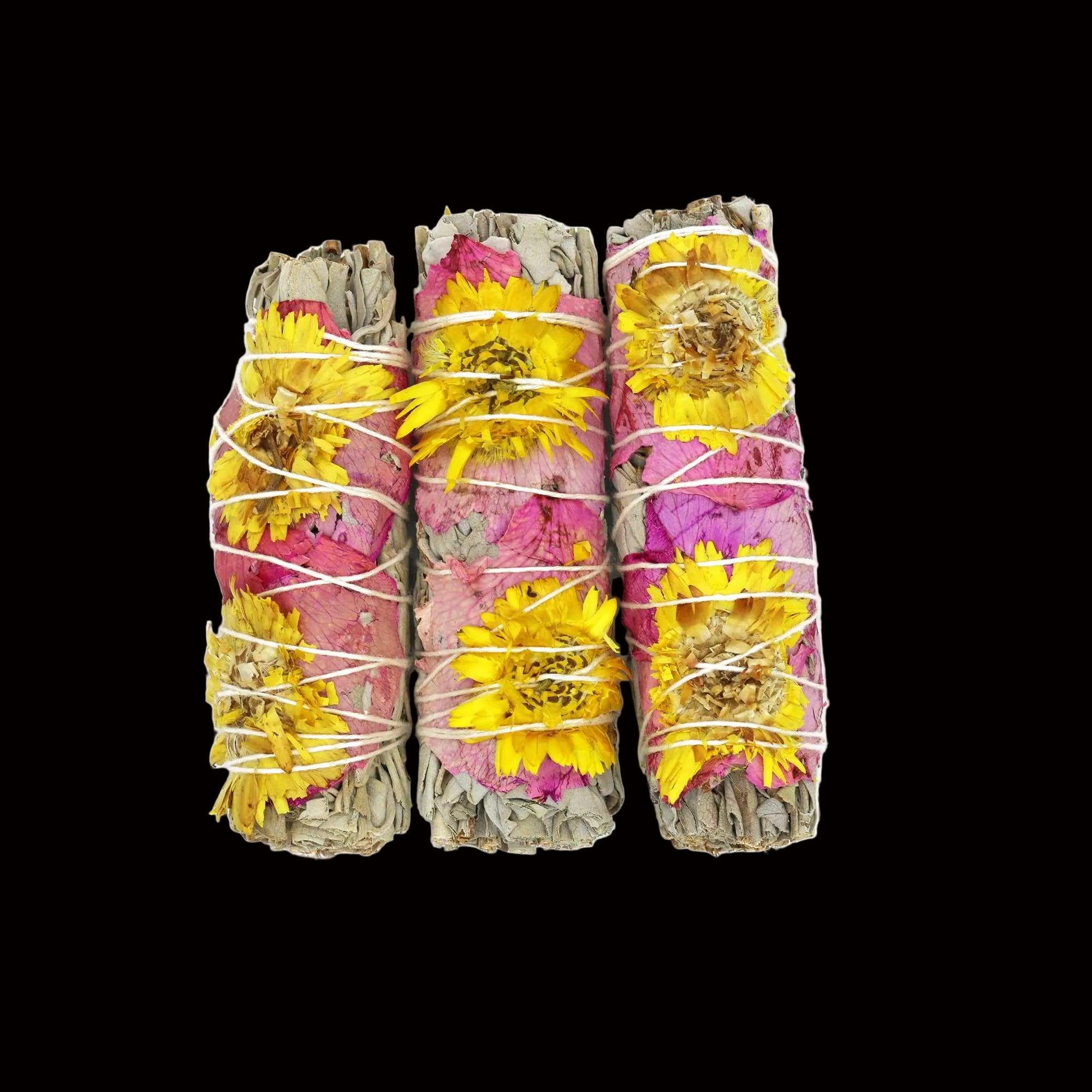 Three bundles of dried flowers and herbs tied together with twine on a white background