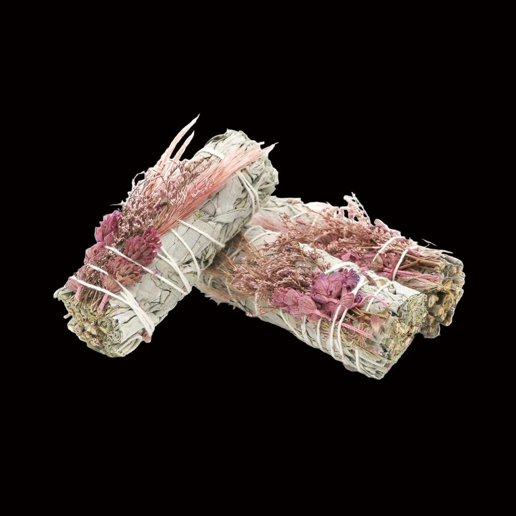 Two bundles of dried herbs tied with pink string on a white background