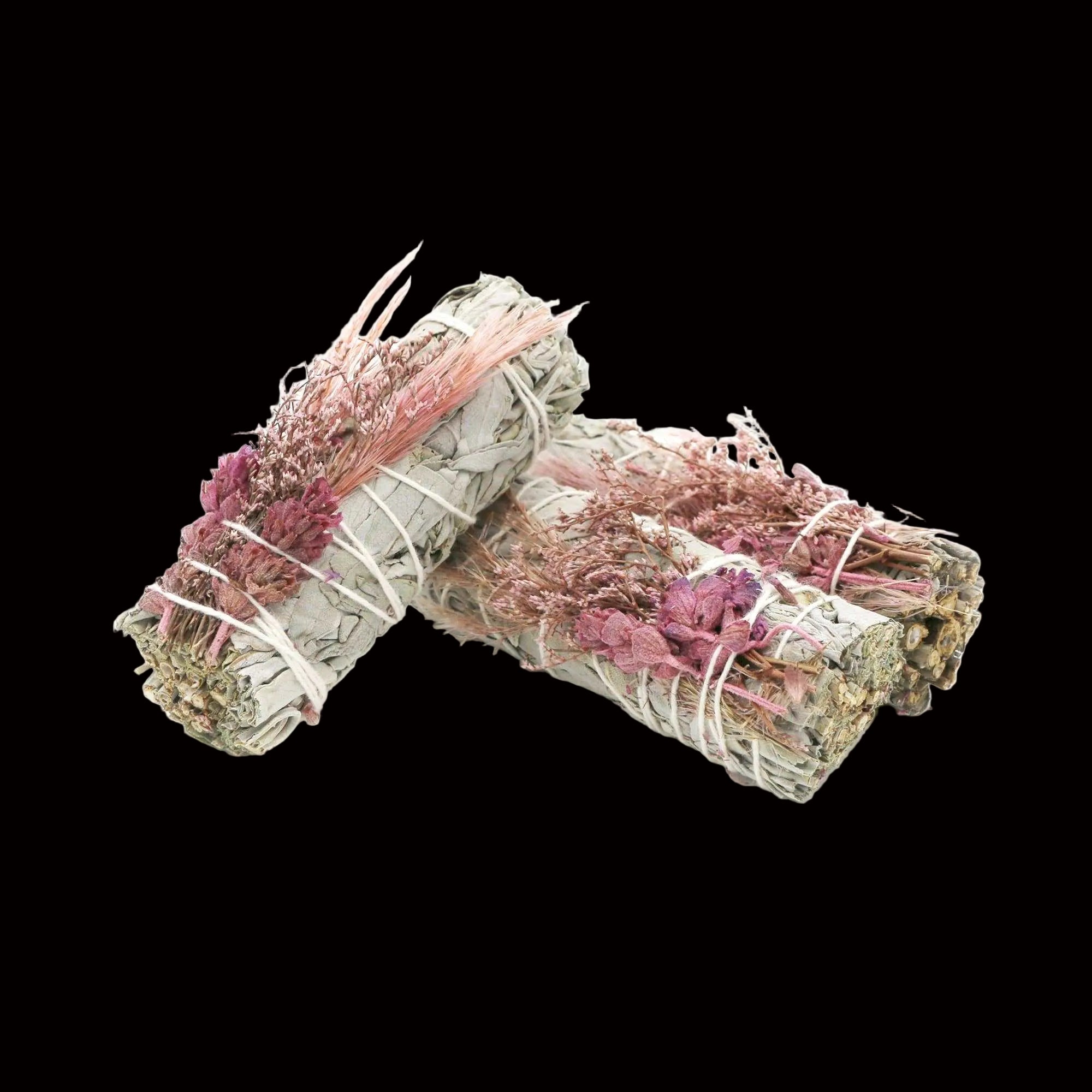 Two bundles of dried herbs tied with pink string on a white background