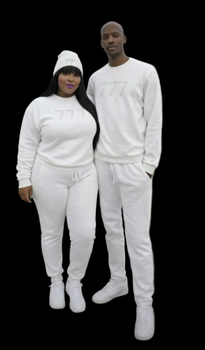 Two people wearing matching white outfits with '777' branding, standing by a waterfront with city skyline in the background.