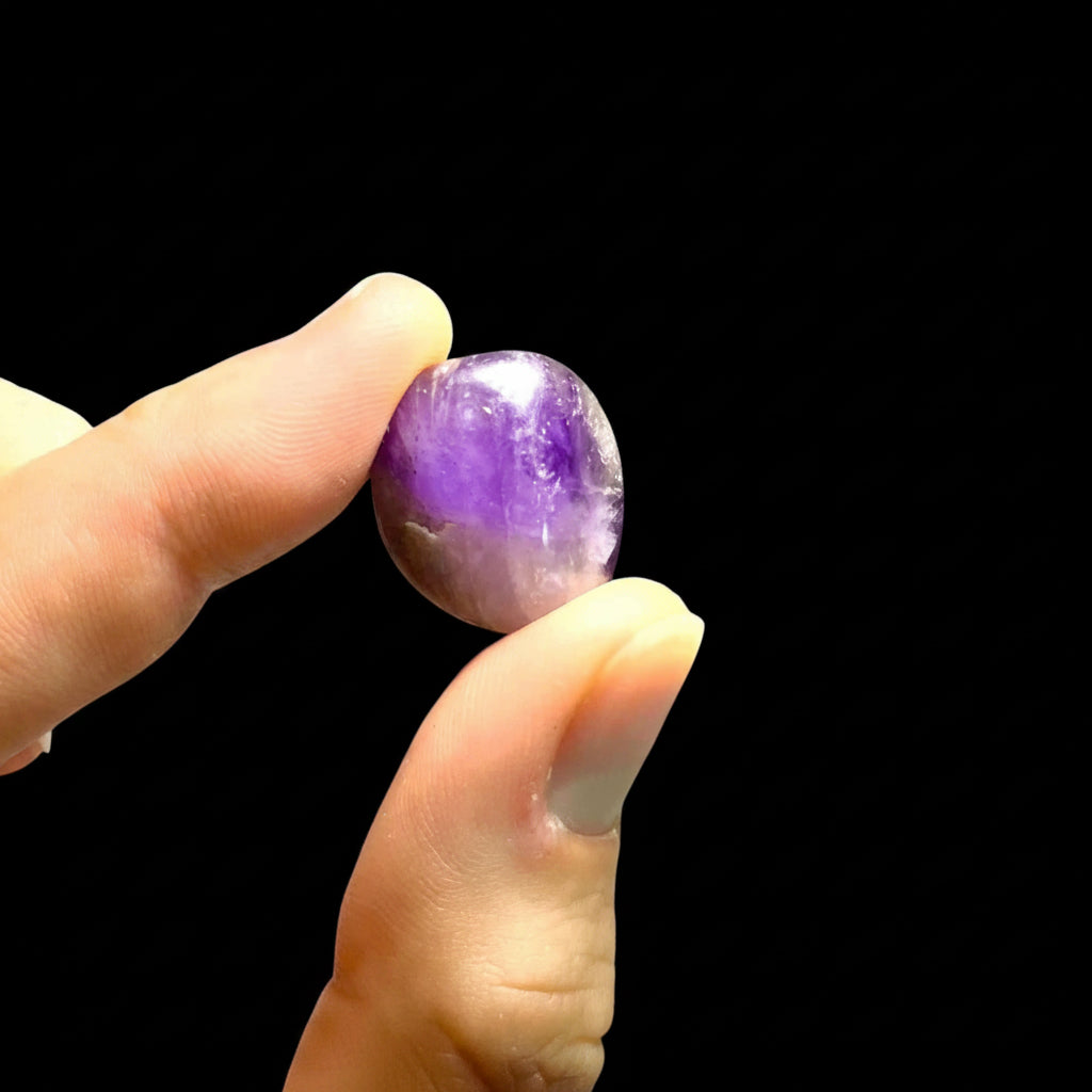 Hand holding a purple crystal against a black background