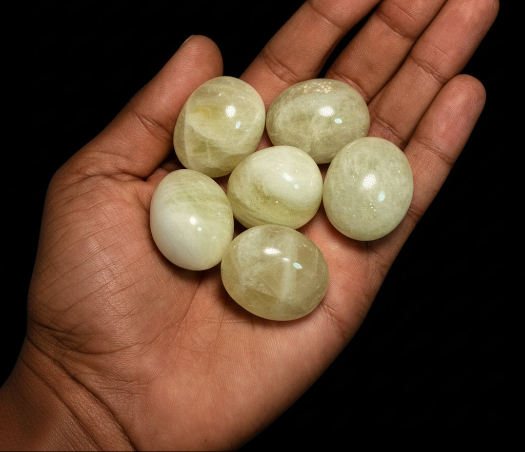 Hand holding five light green stones against a black background