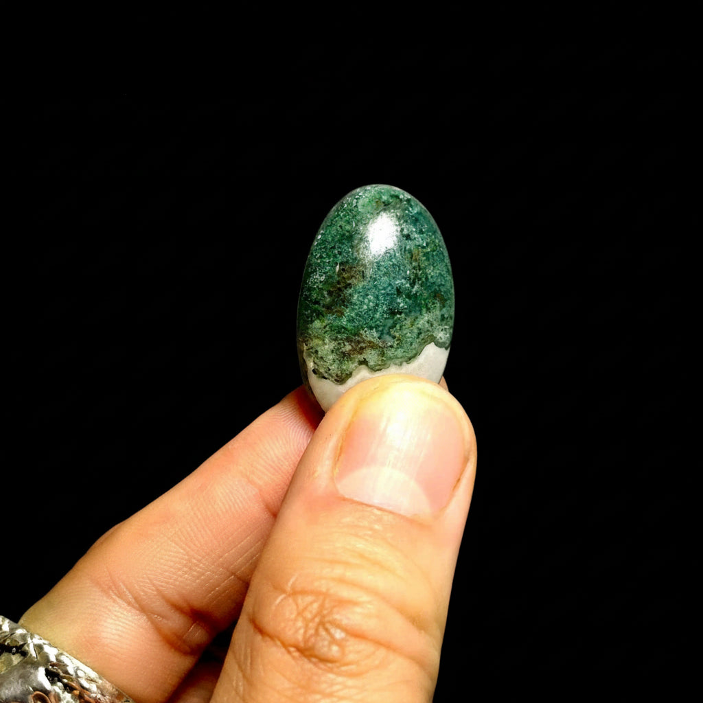 Hand holding a green stone against a black background