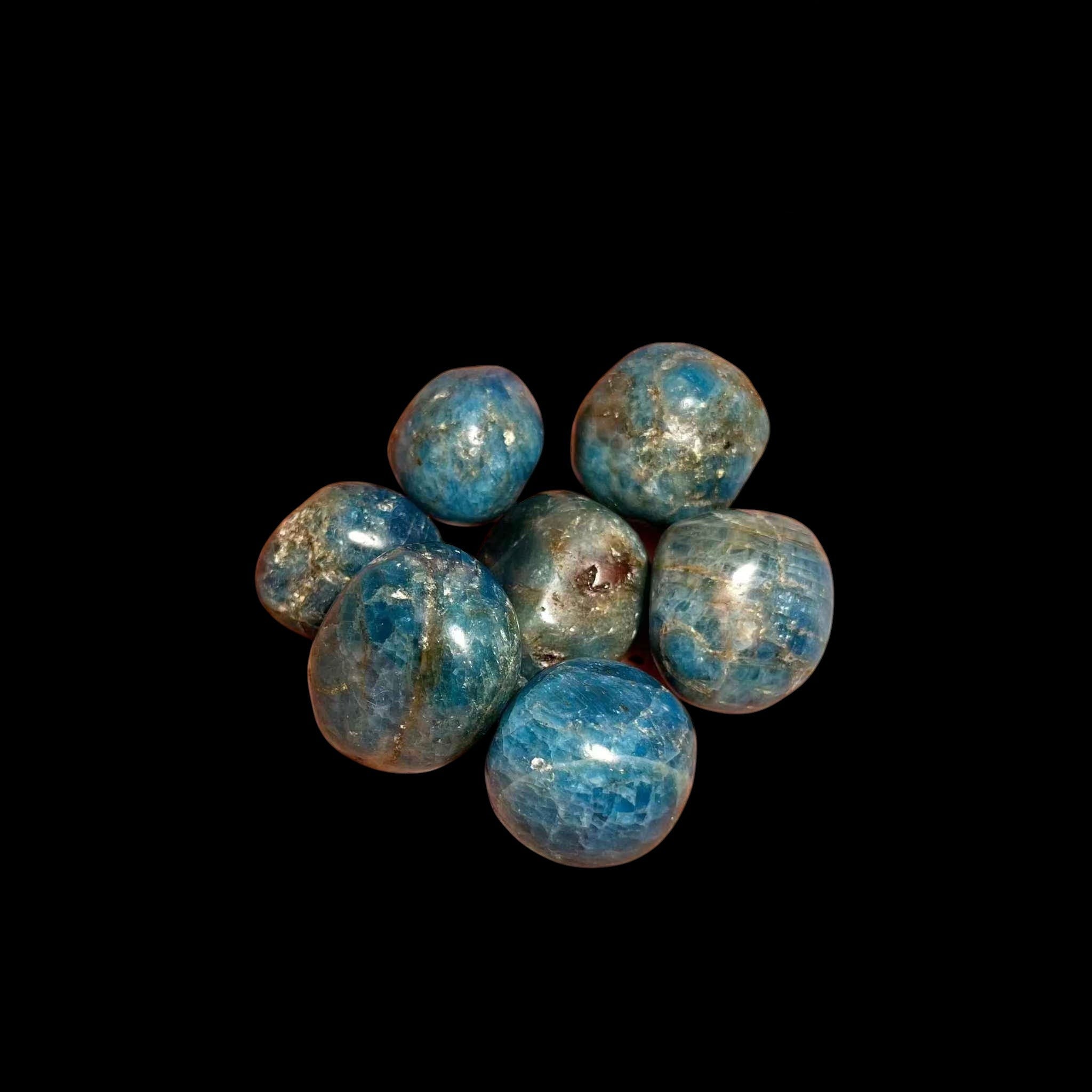 Blue stone beads on a black background with a hand reaching towards them.
