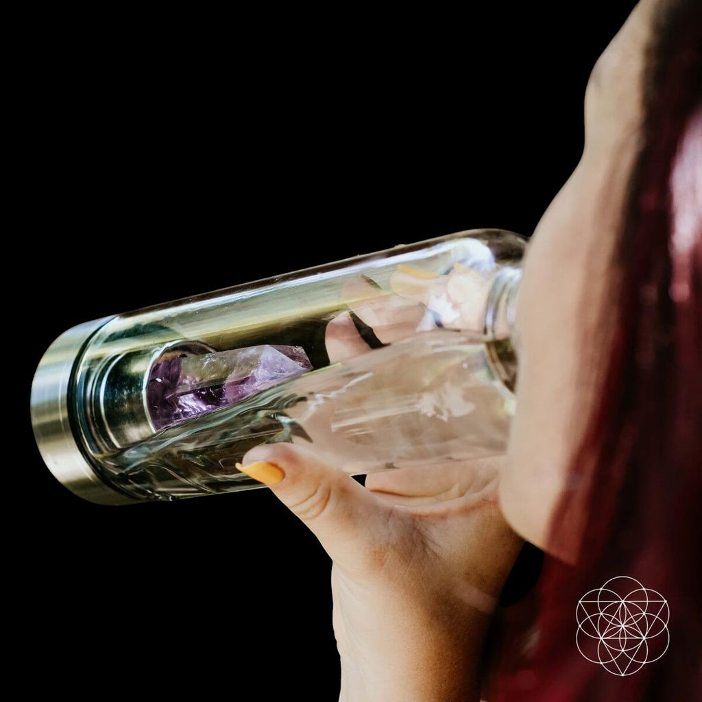 AetherLux™️ glass water bottle with amethyst crystal infusion, held by a person drinking.