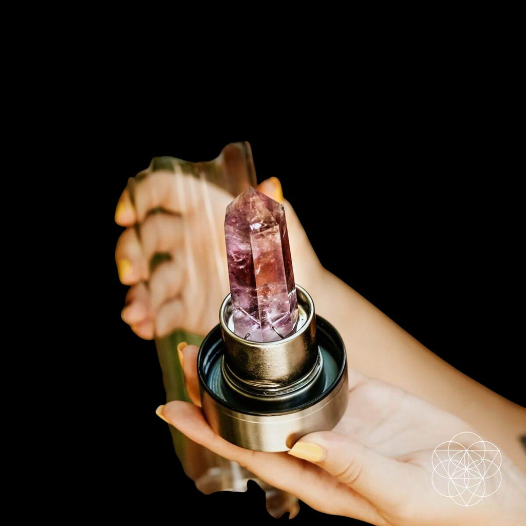 AetherLux™️ healing water bottle with a polished amethyst crystal point inside. The crystal is purple and pink, set in a silver metal holder.