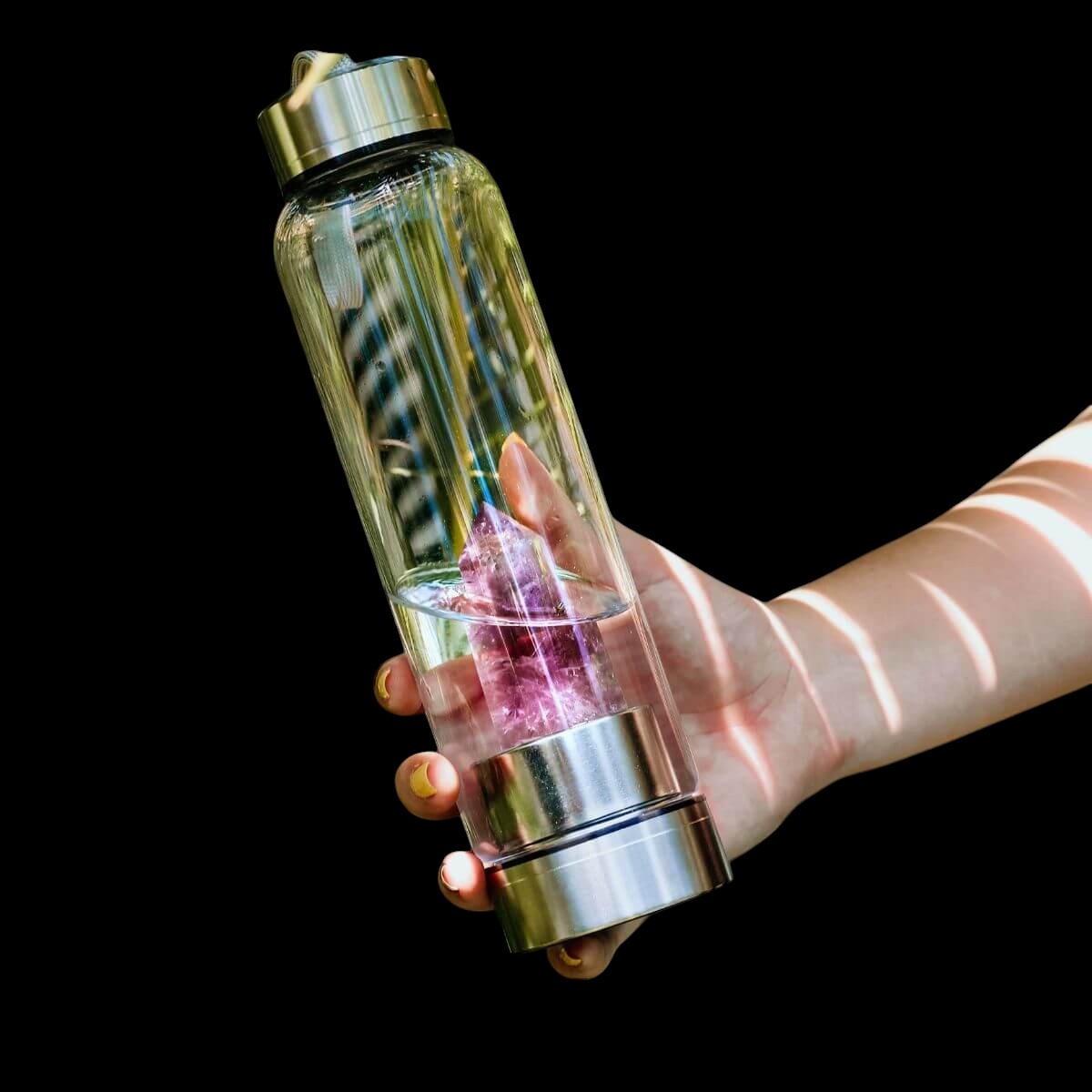 AetherLux™️ glass water bottle with a large amethyst crystal inside, held by a hand.